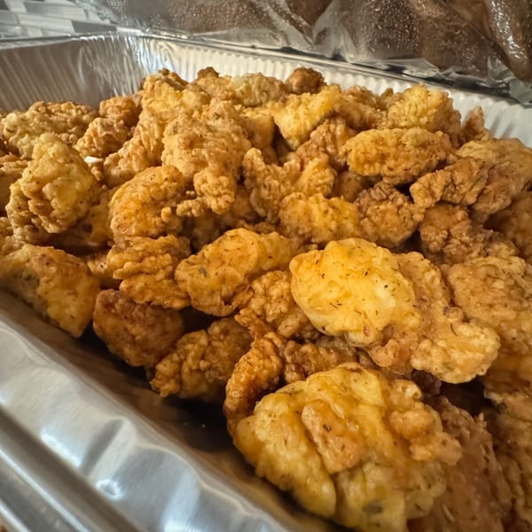 Close-up of golden-brown fried chicken pieces in a large silver catering tray.
