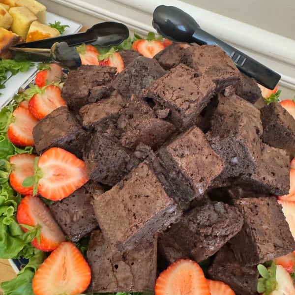 A platter of brownies and sliced strawberries on a bed of lettuce with serving tongs.